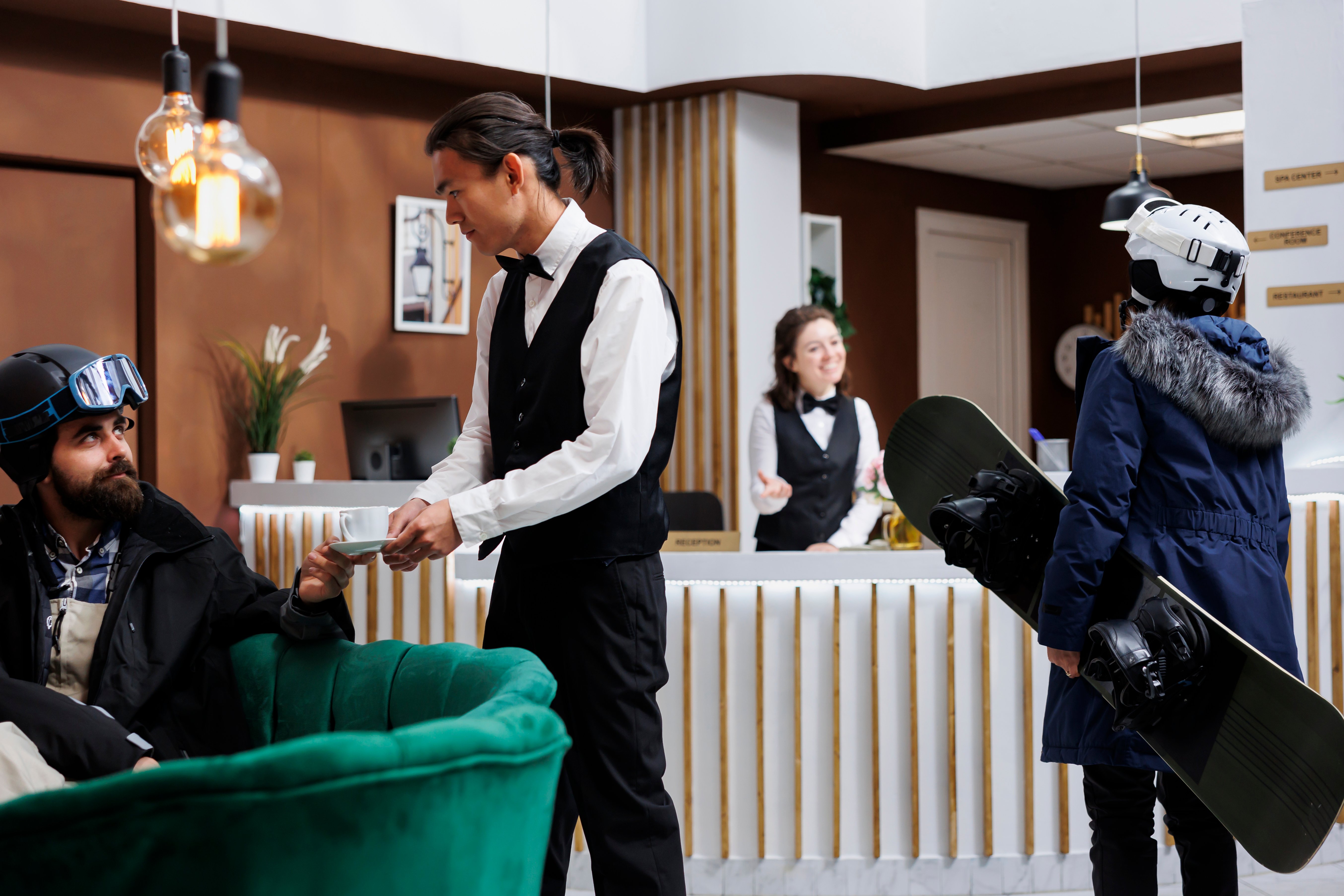 arrival-female-tourist-carrying-snowboard-hotel-lobby-checkin-with-staff-young-waiter-serving-coffee-man-sofa-winter-holiday-atmosphere-with-ski-gear-ski-resort-ensures-happy-stay