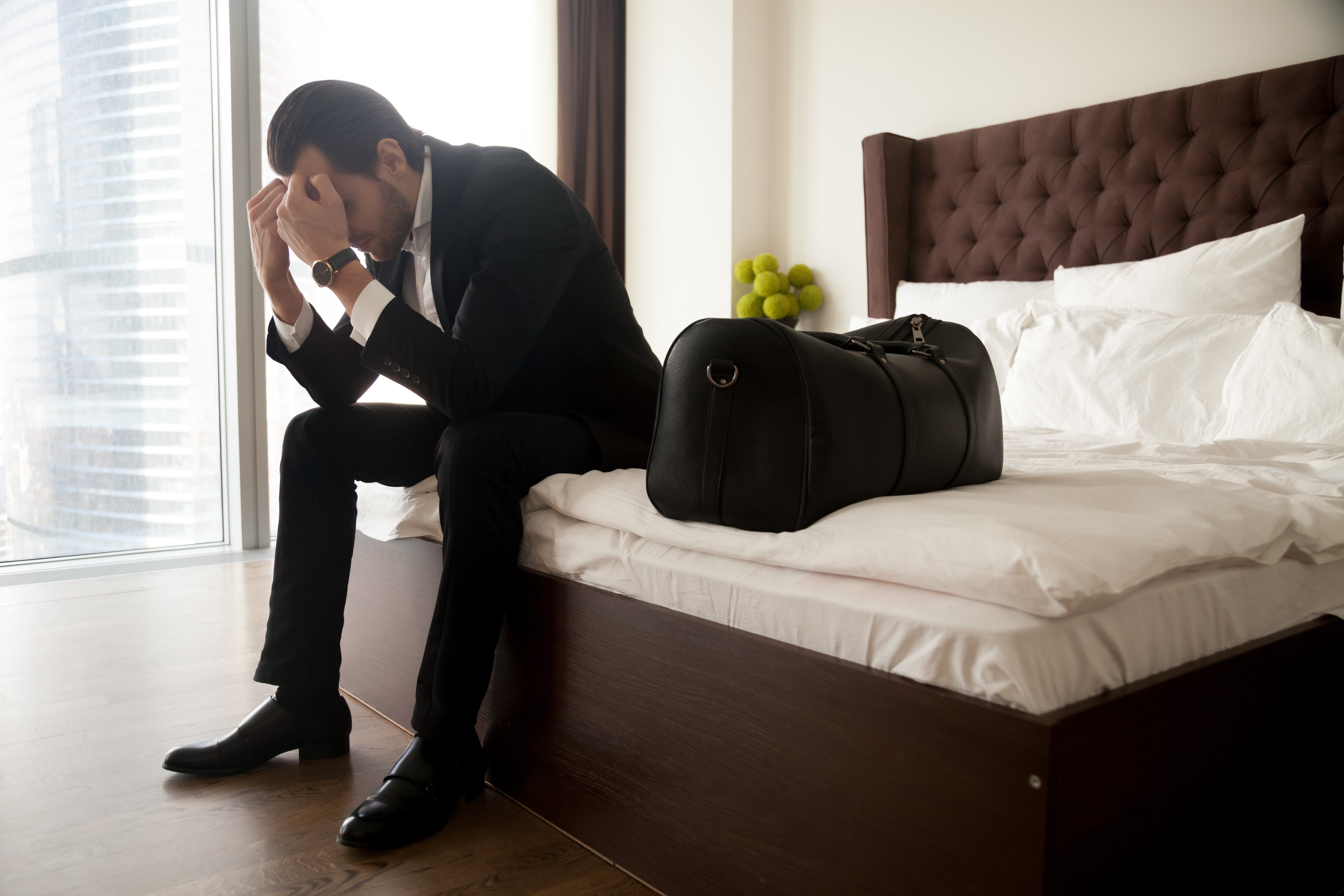 frustrated-man-suit-sitting-bed-besides-luggage-bag